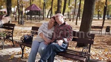 成年儿子在秋天公园坐在长凳上的智能手机上拍摄<strong>年迈</strong>的父母的照片。